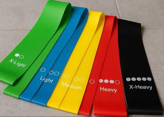 Set of resistance bands in various colors on a tiled floor with a kettlebell and foam roller.
