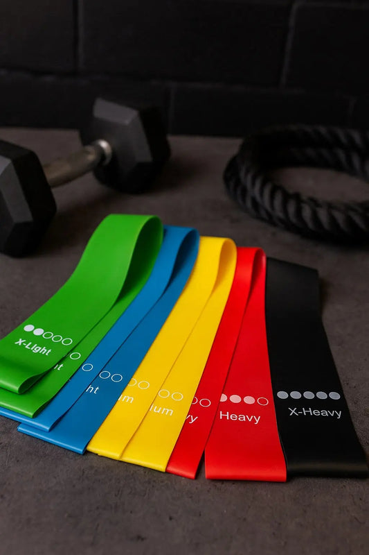 Set of resistance bands in various colors on a dark surface with gym equipment in the background.